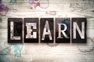 The word "LEARN" written in vintage dirty metal letterpress type on a whitewashed wooden background with ink and paint stains.
